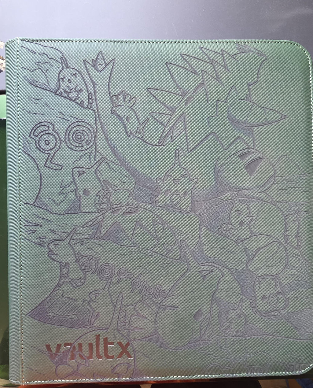 May include: A sage green card binder featuring a debossed graphic of various creatures and rock formations on the front cover. The brand name vaultx is printed in the bottom left corner in a dark font. The cover has a textured, matte finish.