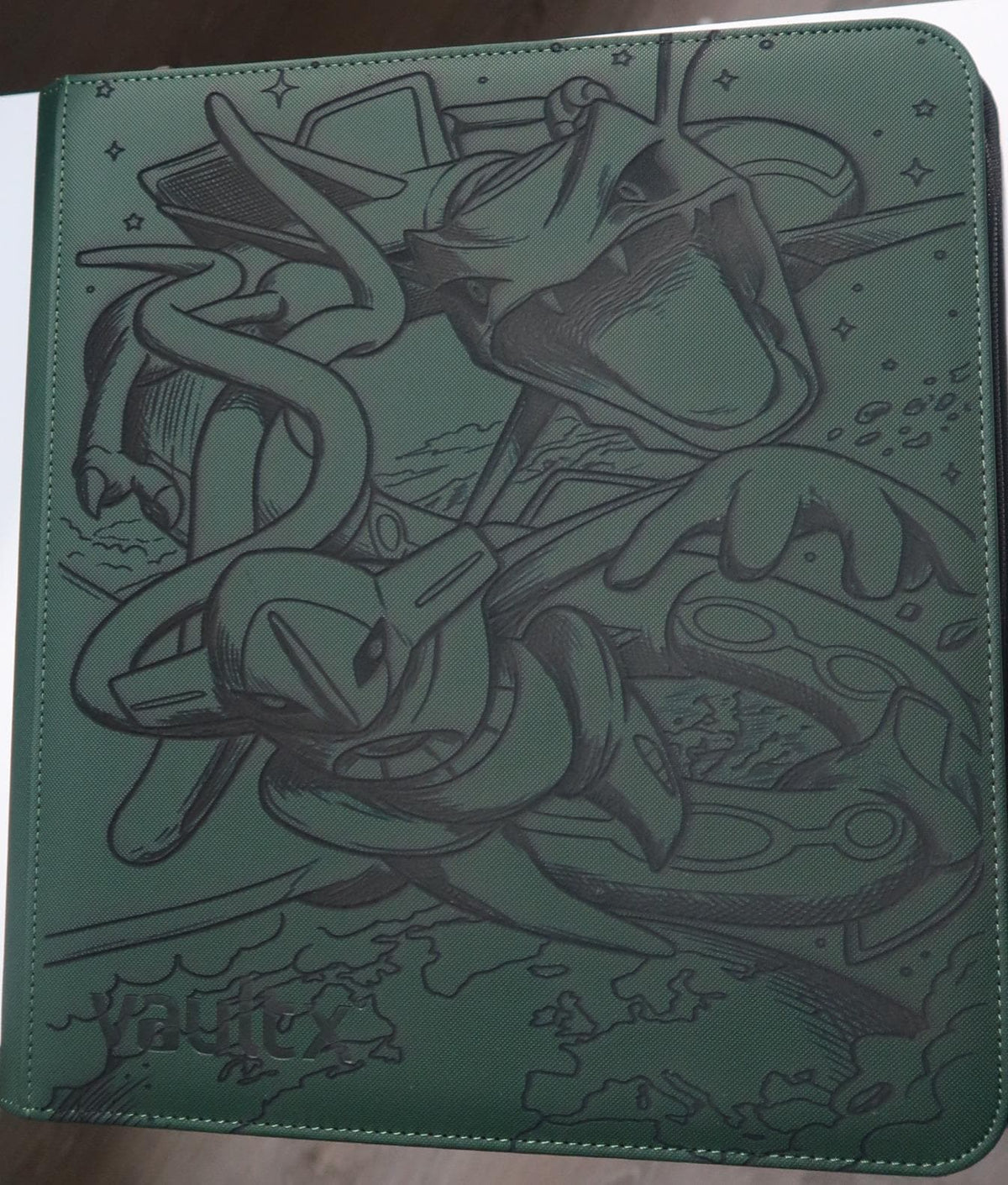 May include: A dark green rectangular trading card binder featuring a black line art illustration of the legendary dragon-type creature Rayquaza. The cover displays the embossed text Vault X in the bottom left corner and includes star motifs.